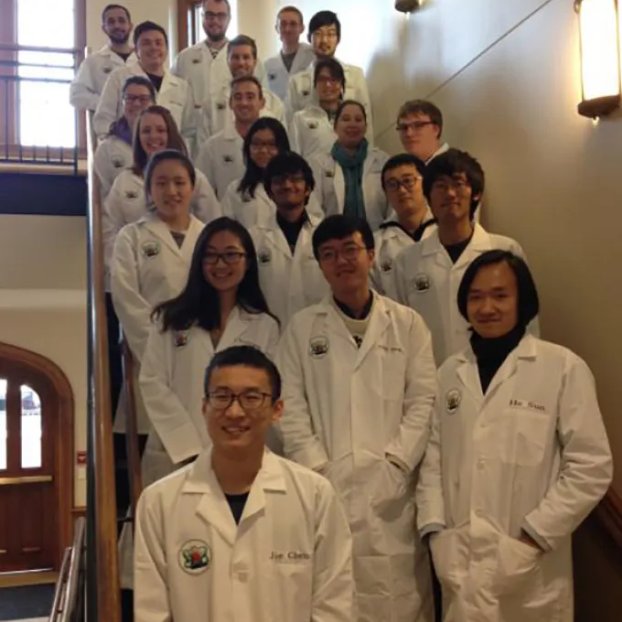 students in white lab coats pose on a staircase